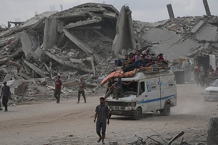 Displaced Palestinians ride on a van loaded with their belongings amid rubble in Gaza City, Sunday, Oct. 12, 2025, after Israel and Hamas agreed  for a ceasefire