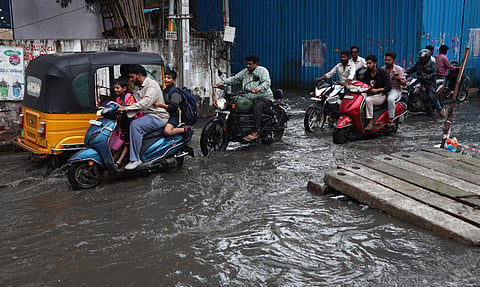 Commuters find it difficult to pass through the road as overflowing rainwater inundates the streets at Krishna Nagar in Yousufguda in Hyderabad. 