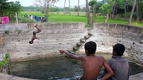 Children are seen joyfully bathing and diving into a village well