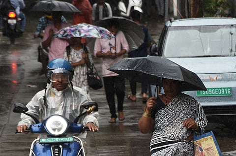 People cover themselves using umbrellas amidst rain at Somajiguda in Hyderabad. 