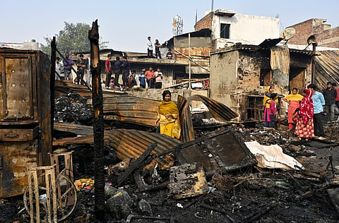 A woman stands amid charred remains after a fire broke out spreading to around 500 shanties near Rithala metro station, at Rohini area, in New Delhi, early Saturday, Nov. 8, 2025. Police said several LPG cylinders were said to have exploded late Friday evening, intensifying the blaze and triggering panic among residents.