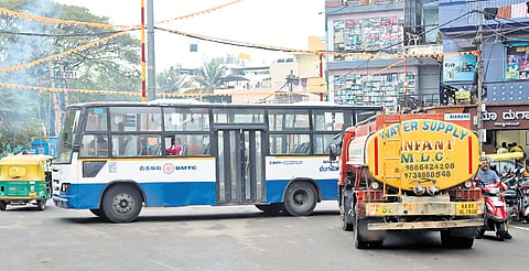A BMTC bus blocks the entire road at Ejipura Circle while trying to make a U-turn, disrupting traffic at the narrow junction 