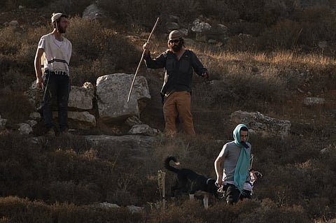 Israeli settlers walk down a hill as Israeli soldiers block access for Palestinians to an area for harvesting olives in the West Bank village of Sa'ir, near Hebron, Thursday, Oct. 23, 2025.