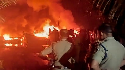Police personnel at the site as smoke and flames billow after fishing boats caught fire, at Ashtamudi Lake in Kollam, Kerala, early Sunday, Dec. 7, 2025. 