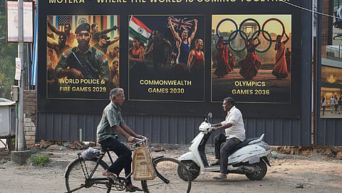People ride past residential project boards featuring upcoming sports events, on the eve of the Commonwealth Sport General Assembly in Glasgow for formal approval of host city, in Ahmedabad, India.