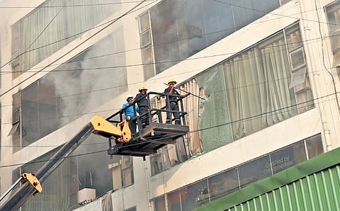 Firefighters use a crowbar to break the glass and douse the fire that broke out at a furniture shop at Nampally in Hyderabad.