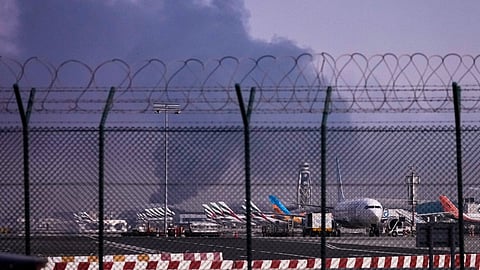 Planes are parked at Dubai International Airport as smoke rises in the background after a drone struck a fuel tank early morning, forcing the temporary suspension of flights, in Dubai, United Arab Emirates, Monday, March 16, 2026. 