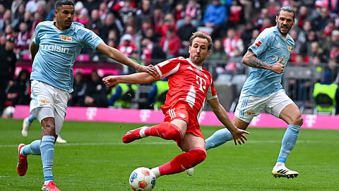 Munich's Harry Kane, center, and Berlin's Livan Burcu, left, challenge for the ball during the German Bundesliga soccer match between FC Bayern Munich and 1. FC Union Berlin in Munich, Germany, Saturday, March 21, 2026 