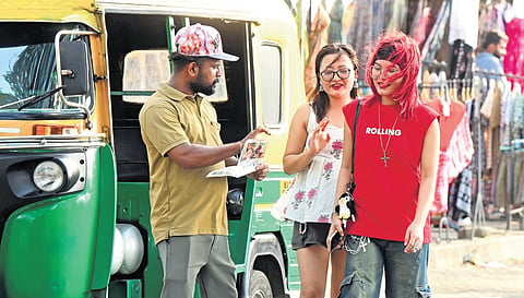 An autorickshaw driver shows a brochure listing popular destinations in the area to tourists near the water metro station in Fort Kochi.