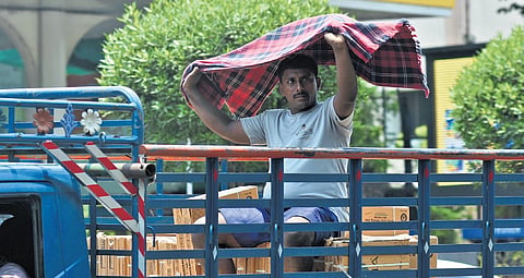 Covering himself with a towel, a worker travelling on a cargo auto on a sunny afternoon in Vijayawada on Tuesday 