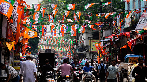 Commuters pass through a busy street decorated with the flags of Bharatiya Janata Party and Trinamool Congress party ahead of the West Bengal state Legislative Assembly elections in Kolkata, Saturday, April 18, 2026. 