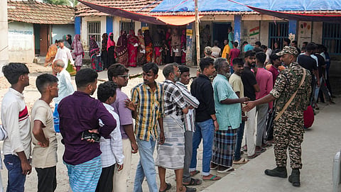 A security official stands guard as people wait in a queue to cast votes during the first phase of the West Bengal Assembly election, in Nandigram, Purba Medinipur district, Thursday, April 23, 2026. 