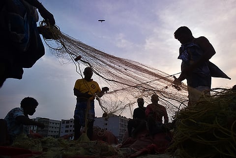 Fishermen are seen mending and sorting fishing nets along the shore 