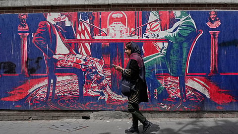 A woman walks past an anti-U.S. mural painted on the wall of the former U.S. embassy mocking Iran and United States talks, in Tehran, Iran, Saturday, April 25, 2026. 