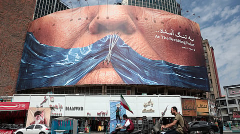 Motorists ride past an anti-US billboard referring to President Donald Trump and the Strait of Hormuz, installed on a building at the Valiasr Square in Tehran on May 2, 2026.