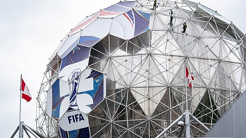 Workers drop from the top of Science World to install a football wrap for the 2026 FIFA World Cup football tournament in Vancouver, British Columbia, Wednesday, May 13, 2026.