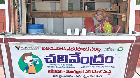 Holding a hand fan for comfort, a woman sits in a VMC water kiosk on a sunny afternoon in Vijayawada 
