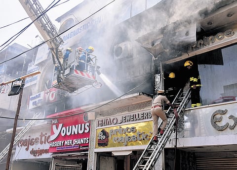 Firefighters try to douse the flames as smoke billows out the clothing store on fire in the Madina market area, Hyderabad, on Thursday.