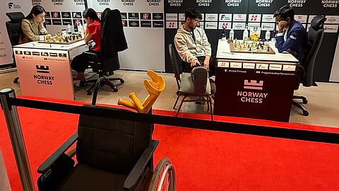 Alireza Firouzja with his injured right ankle resting on another chair during his match against R Praggnanandhaa on Tuesday. In the foreground, the wheelchair with which he was brought to the venue is visible 