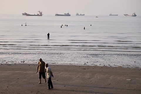 Men walk on the shoreline as people wade in the water in the Strait of Hormuz, where cargo and service vessels are anchored off Bandar Abbas, Iran, Monday, June 1, 2026. 