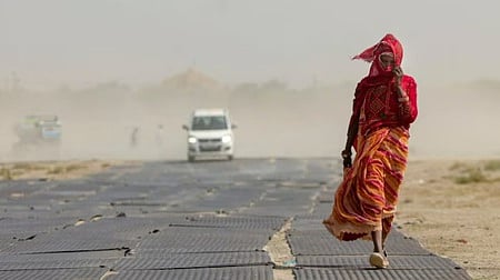 A woman covers her face while walking along a road amid dusty winds and scorching heat during a heatwave in Prayagraj. 
