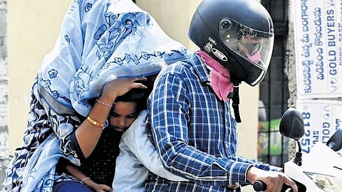 A family of four rides on a two-wheeler while shielding themselves from the harsh afternoon sun with a shawl in Karimnagar.