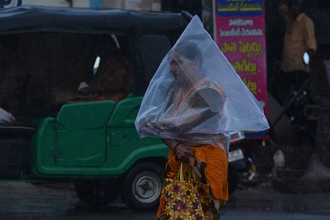 A woman covers herself with plastic cover during sudden downpour in Vijayawada on Friday.