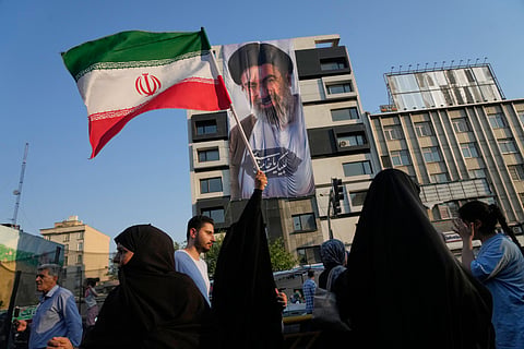 A woman holds up an Iranian flag in front of a banner showing a portrait of the Supreme Leader Ayatollah Mojtaba Khamenei during a street festival in Tehran