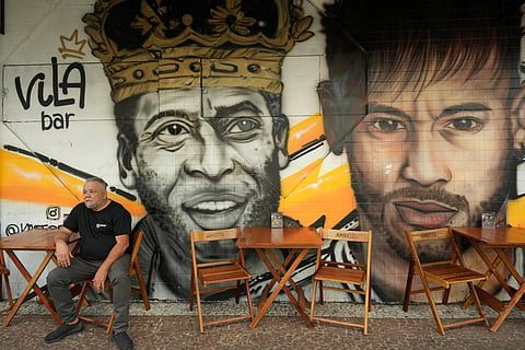 A man sits in front of a mural of late football legend Pele and Neymar at a restaurant in Santos, Brazil.