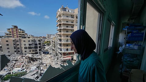 A nurse looks through a shattered window of the Jabal Amel Hospital into a destroyed building that was hit Monday in an Israeli airstrike, in the southern port city of Tyre, Lebanon on June 2, 2026