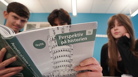 High school students from left, Vasilije Stjepanovic, Aslan Ozhan Kilicasan and Melina Sallahi pose with a history text book at Malmo Borgarskola high school in Malmo, Sweden, May 21, 2026.