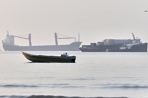 A small boat moves along the shoreline where an a cargo vessel, tugboat and industrial barge are all anchored in the Strait of Hormuz off Bandar Abbas, Iran, Monday, June 1, 2026.