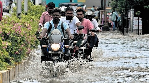 Two-wheeler riders wade through a water logged road.