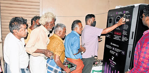 People stand in a queue to deposit empty liquor bottles in a bottle deposit machine at a Tasmac shop in Egmore