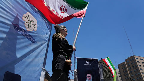 A woman waves an Iranian flag during a pro-government campaign as a portrait of the slain Supreme Leader Ayatollah Ali Khamenei, who was killed in US and Israeli strikes on Feb. 28, is displayed at right in downtown Tehran, Iran, Monday, June 15, 2026. 