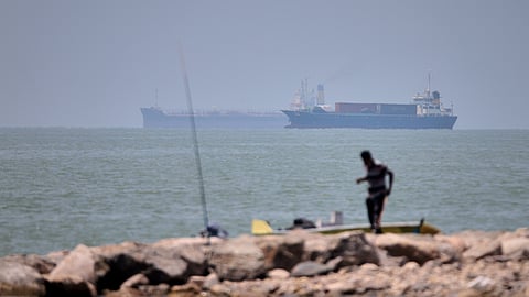 A man stands beside a fishing pole along the shore as cargo ships and commercial vessels are seen in the Strait of Hormuz off Bandar Abbas, Iran, Wednesday, June 17, 2026. 