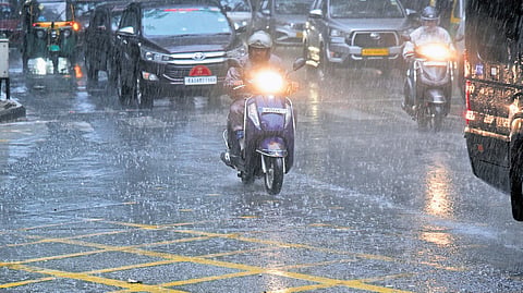 Vehicles make way through a rain-soaked road after a sudden burst of rain in Shivajinagar, Bengaluru, on Monday evening.