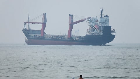 A group of people stand in shallow water as a cargo ship appears anchored in the Strait of Hormuz off Bandar Abbas, Iran, Tuesday, June 30, 2026
