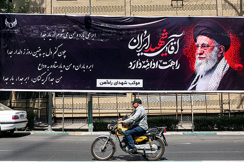 A man rides a motorcycle past a mourning banner depicting Iran's slain supreme leader Ali Khamenei, who was killed in a strike on the first day of the US-Israeli war against the Iran on February 28, in Tehran on June 30, 2026 ahead of his public funeral.