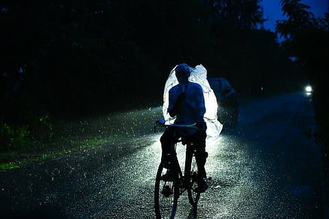 A man wraps a plastic sheet around while cycling through drizzle on Canal Road near Jagatpur in Cuttack. 