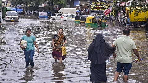 People wade through a waterlogged road at Ved Darwaja after heavy rainfall, in Surat