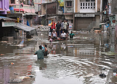 People use a boat to cross a waterlogged area following heavy rain, in Surat, Thursday, July 9, 2026.