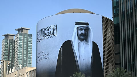 A photograph shows a billboard bearing a portrait of Qatar's former leader Sheikh Hamad bin Khalifa Al Thani in Doha on July 12, 2026, after the announcement of his death.