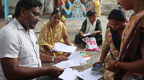 A booth-level officer verifies the enumeration forms submitted by a resident for the Special Intensive Revision (SIR) roll.
