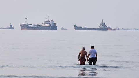Two men wade in the waters of the Strait of Hormuz with vessels anchored in the background, off Bandar Abbas, Iran, Sunday, July 12, 2026.