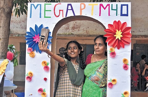 Parents and students participate in photo booth activities, musical chairs and pose with placards highlighting educational schemes during the Mega PTM at AKTP School in Vijayawada.