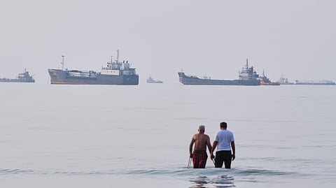Two men wade in the waters of the Strait of Hormuz with vessels anchored in the background, off Bandar Abbas, Iran, Sunday, July 12, 2026.