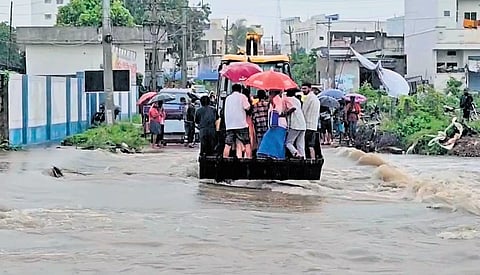 A JCB carries people across a flooded road at Venkatadrinagar of Govindayapally in Jagtial district 