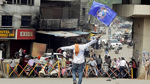 A protestor waves a flag near a barricade installed to stop traffic movement towards the Bhandari Bridge as it is closed by sanitation workers during a call for Punjab Bandh, in Amritsar on Thursday, July 30, 2026.