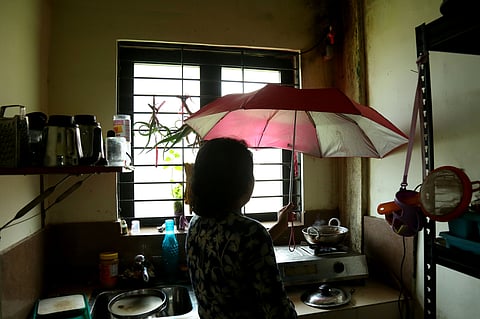 A woman cooking food inside a leaking kitchen under the cover of an umbrella